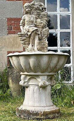 Grande fontaine d'eau en cascade assise avec une jeune fille de campagne tenant un panier de fruits.