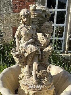 Grande fontaine d'eau en cascade assise avec une jeune fille de campagne tenant un panier de fruits.